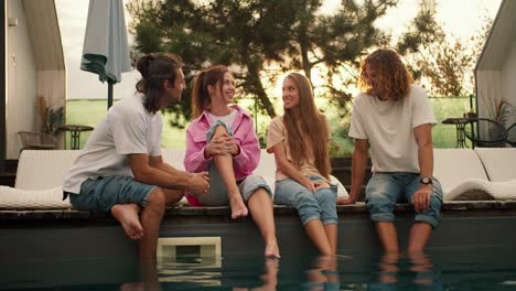 Cuatro-Amigos-Se-Sientan-Cerca-De-Las-Tumbonas-Junto-A-La-Piscina-Y-Se-Divierten-Charlando-Entre-Ellos-Con-El-Atardecer-De-Fondo.-Descanso-En-La-Casa-De-Campo.