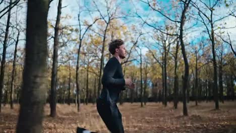 Shot-from-the-side-a-man-with-curly-hair-in-a-black-sports-uniform-and-a-beard-runs-through-the-autumn-forest-wipes-sweat-from-his-forehead-and-smiles-looking-around-in-the-morning