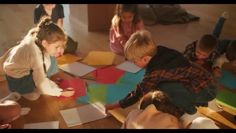 Preschool-children-on-the-floor-draw-on-multi-colored-paper-using-multi-colored-pencils-in-a-club-to-prepare-children-for-school.-Happy-children-in-a-sunny-room-draw-on-the-floor-on-colorful-paper-using-pencils