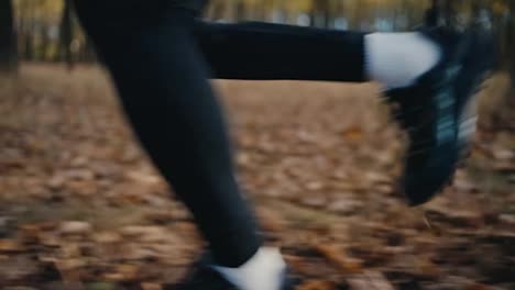 Close-up-shot-of-a-man-in-a-black-sports-uniform-with-white-socks-and-black-sneakers-running-along-a-seed-path-in-the-autumn-sunny-forest-during-his-jog-in-the-morning