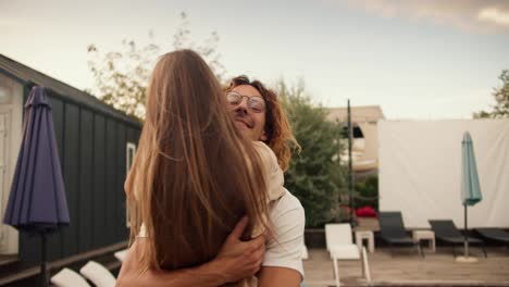 Close-up-shooting:-A-girl-with-long-hair-rides-her-curly-haired-boyfriend-in-glasses-and-hugs-him-near-the-sunbeds-by-the-pool.-Rest-in-the-country-house