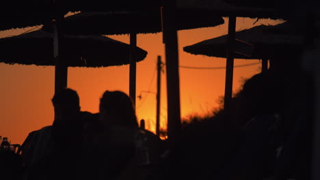 Menschen-Entspannen-Sich-Am-Strand-Bei-Sonnenuntergang,-Schwarze-Silhouetten-Auf-Orangefarbenem-Himmelshintergrund