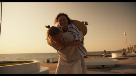 A-happy-girl-in-a-white-and-blue-shirt-approaches-her-boyfriend-from-behind-and-he-lifts-her-into-his-arms-on-a-beach-with-palm-trees-near-the-sea-at-dawn-in-summer.-Happy-couple-guy-and-girl-fooling-around-on-the-beach-near-the-sea