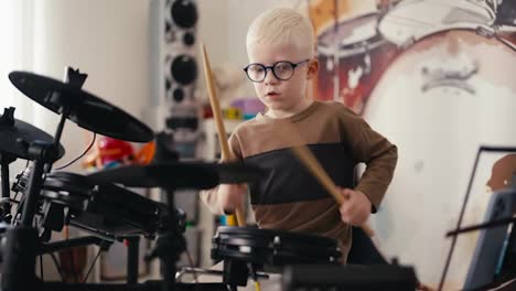 Ein-Kleiner-Talentierter-Albino-Junge-Mit-Weißem-Haar-Und-Runder-Blauer-Brille-Spielt-In-Seiner-Freizeit-Tagsüber-In-Seinem-Zimmer-Ein-Elektronisches-Trommelmusikinstrument-Mit-Speziellen-Holzstöcken