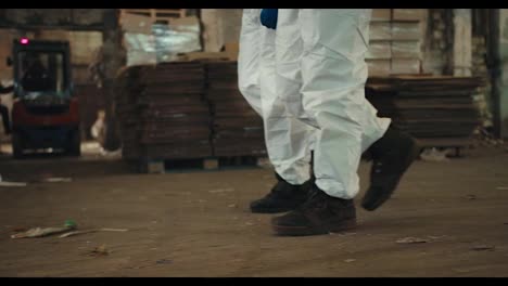 Close-up-shot-of-two-engineer-employees-in-white-protective-uniforms-and-black-shoes-walking-along-a-plant-for-recycling-waste-paper-and-plastic