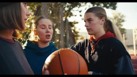 Close-up-three-blonde-girls-in-sportswear-communicate-with-each-other-with-a-basketball-and-stand-on-a-street-court-on-a-sunny-day-in-summer