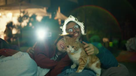 Primer-Plano:-Una-Pareja-De-Enamorados-Tumbados-En-Un-Puf,-Acariciando-A-Un-Gato-Rojo-Y-Viendo-Una-Película.-Fiesta-Fuera-De-La-Ciudad.-Descanso-En-Una-Casa-De-Campo.