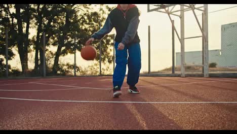 A-blonde-girl-in-a-sports-uniform-maneuvers-with-the-ball-bouncing-it-off-the-floor-during-her-game-of-basketball-on-the-Red-street-court-in-the-summer-morning