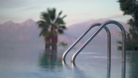 Open-pool-with-shiny-railing-against-palm-trees-and-mountains