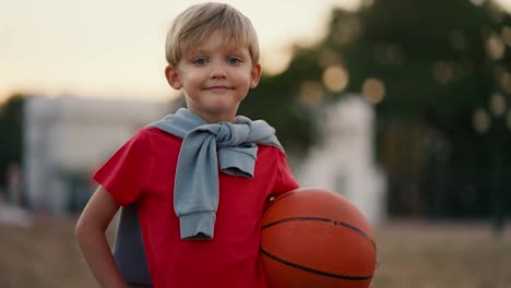 Porträt-Eines-Glücklichen-Kleinen-Blonden-Jungen-Mit-Blauen-Augen-In-Einem-Roten-T-Shirt-Mit-Einem-Basketball-Im-Park.-Glücklicher-Kleiner-Junge,-Der-Spaß-Hat-Und-Sportspiele-Im-Park-Spielt