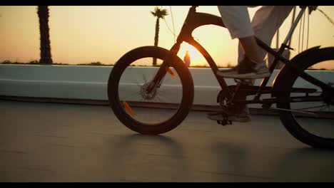 Ein-Glücklicher-Mann-In-Weißen-Hosen-Tritt-In-Die-Pedale-Und-Fährt-Mit-Seinem-Schwarzen-Fahrrad-Am-Morgenstrand-Entlang-Des-Meeres-Bei-Sonnenaufgang-Im-Sommer