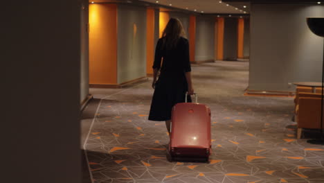 Woman-with-suitcase-walking-to-the-room-in-hotel-corridor