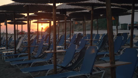 Sunset-scene-of-beach-with-straw-umbrellas-and-empty-chaise-longues