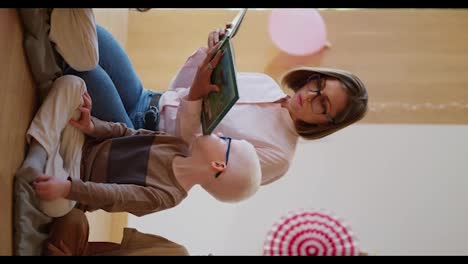 Vertical-video-of-a-woman-with-a-bob-hairstyle-in-glasses-in-a-pink-shirt-reading-a-green-book-for-her-students-of-preschool-children-in-a-club-for-preparing-children-for-school