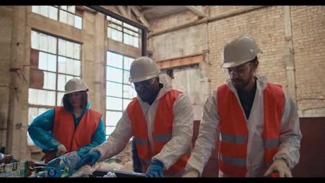 Un-Trío-De-Trabajadores-De-Fábrica-Con-Uniformes-Blancos-Especiales,-Chalecos-Naranjas-Y-Cascos-Blancos-Reciclan-Basura-Y-Botellas-De-Plástico-En-Una-Cinta-Transportadora.