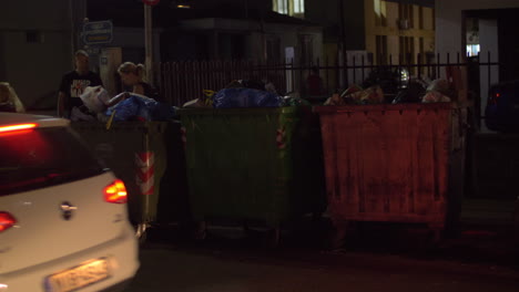 Calle-De-La-Ciudad-Con-Vista-Nocturna-De-Contenedores-De-Basura-Llenos.