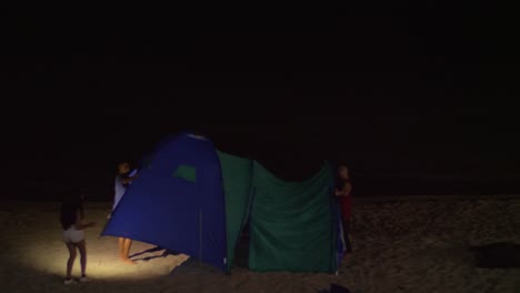 Jóvenes-Levantando-La-Tienda-De-Campaña-En-La-Orilla-Del-Mar-Por-La-Noche.