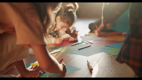 Close-up-shooting-of-preschool-children-sitting-on-the-floor-and-drawing-on-multi-colored-paper-using-pencils-in-a-club-for-preparing-children-for-school