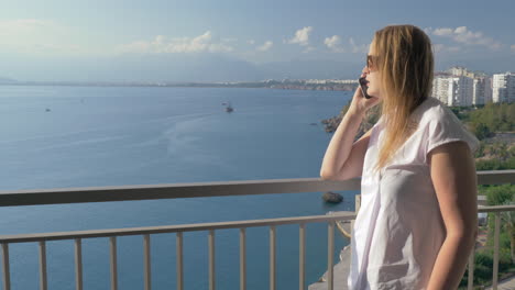 Mujer-Hablando-Por-Teléfono-Y-Disfrutando-De-La-Vista-Al-Mar-Desde-El-Balcón.