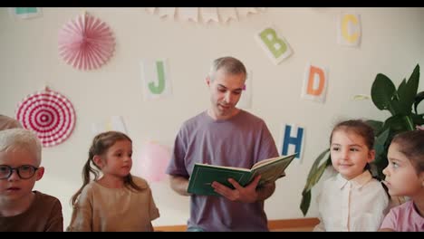 Ein-Mann-In-Einem-Lila-T-Shirt-Mit-Grauen-Haaren-Und-Ein-Mädchen-Mit-Bob-Frisur-In-Einem-Weißen-Hemd-Sitzen-Mit-Kindern-Auf-Dem-Boden-Im-Kreis-Und-Lesen-Ein-Buch.-Der-Mann-Liest-Ein-Buch-Für-Kinder-Im-Vorschulalter