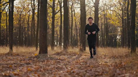 A-man-with-curly-hair-and-a-beard-in-a-black-brunette-sports-uniform-looks-at-his-watch-and-then-runs-quickly-to-his-destination-during-his-sprint-and-jog-in-the-morning-in-the-autumn-forest