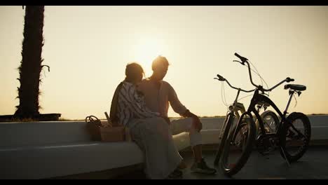 Un-Chico-Y-Una-Chica-Están-Sentados-En-Bancos-Blancos-En-La-Playa-En-La-Que-Crecen-Palmeras-Cerca-De-Ellos,-Sus-Bicicletas.-Un-Chico-Y-Una-Chica-Fueron-En-Bicicleta-A-La-Playa-Y-Descansaron-Allí-Por-La-Mañana-Al-Amanecer.