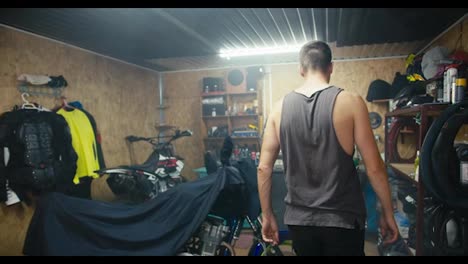 An-experienced-man-mechanic-enters-his-garage-workshop-and-removes-the-cape-from-his-motorcycle.-Start-of-the-working-day-in-the-workshop.-Starting-a-new-job