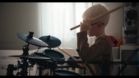 Ein-Kleiner-Albino-Junge-Mit-Weißer-Haarfarbe-Und-Runder-Blauer-Brille-Spielt-Zu-Hause-In-Seinem-Zimmer-Auf-Einem-Elektronischen-Schlagzeug.-Ein-Glücklicher-Kleiner-Junge-Mit-Talent-Für-Das-Spielen-Von-Musikinstrumenten-Hält-Schlagstöcke-In-Den-Händen-Und-Spielt-Schlagzeug.