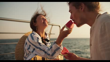 Happy-couple-guy-and-girl-on-a-date-and-on-the-pier-near-the-sea-they-eat-watermelon-and-feed-it-to-each-other.-Couple-on-a-date-near-the-sea-on-a-picnic