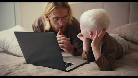 A-happy-albino-boy-with-white-hair-looks-at-his-father-while-watching-an-educational-film-and-asks-him-a-question.-The-man-answers-his-boy-and-tries-to-clarify-all-his-questions