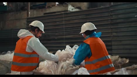 A-brunette-man-with-a-beard-in-a-white-protective-uniform-and-an-orange-vest-together-with-a-brunette-girl-presses-plastic-cellophane-while-working-at-a-waste-processing-and-sorting-plant