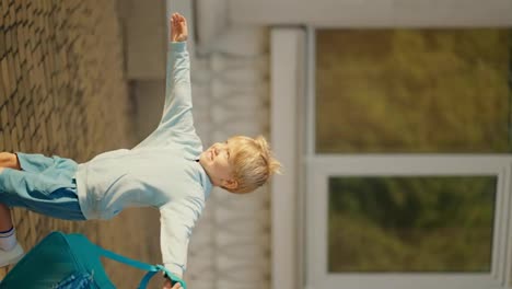 Vertical-video:-A-happy-little-blond-boy-in-blue-clothes-with-a-blue-backpack-runs-from-school-to-his-dad-who-takes-him-in-his-arms,-they-are-very-happy-to-meet