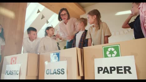 a-blonde-girl-with-a-bob-hairstyle-teaches-preschool-children-how-to-properly-fold-plastic-bottles-and-sort-garbage-by-type-of-material-in-a-club-to-prepare-children-for-school