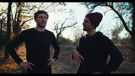 A-brunette-guy-in-a-red-hat-talks-to-his-friend-with-a-beard-in-a-black-sports-uniform-who-tells-him-how-to-properly-go-for-a-morning-jog-in-the-fall-during-sunrise