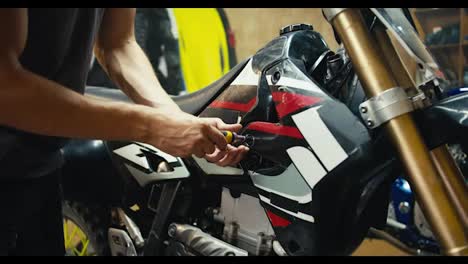 A-male-mechanic-in-a-gray-T-shirt-disassembles-a-motorcycle-using-special-tools.-A-man-with-sinewy-arms-works-in-his-workshop