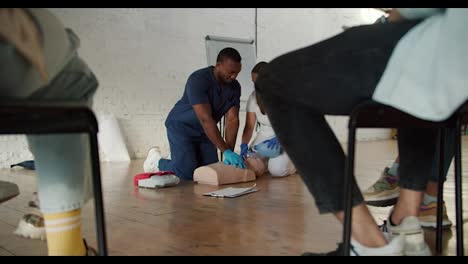 Bottom-view:-A-Black-male-doctor-in-a-blue-uniform-performs-artificial-respiration-for-a-medical-mannequin,-his-assistant-a-female-nurse-in-a-white-uniform-makes-a-mannequin-artificial-respiration-using-an-Anbu-resuscitation-bag