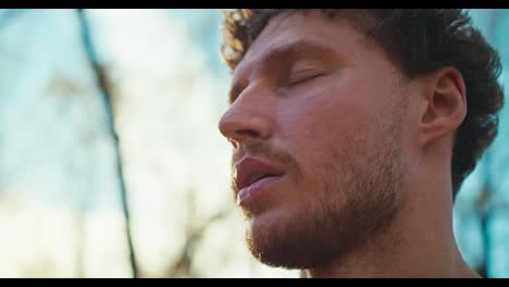 A-calm-and-tired-man-with-curly-hair-and-beard-wipes-sweat-from-his-face-after-a-hard-jog-in-the-morning-in-autumn.-Close-up-shot-of-a-male-athlete-resting-after-a-run-and-wiping-sweat-from-his-face