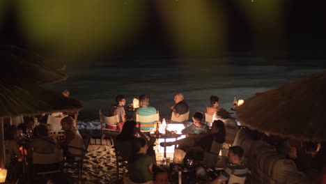 Café-En-La-Playa-Con-Gente-Relajándose-Y-Tomando-Bebidas-Junto-Al-Mar-Por-La-Noche.