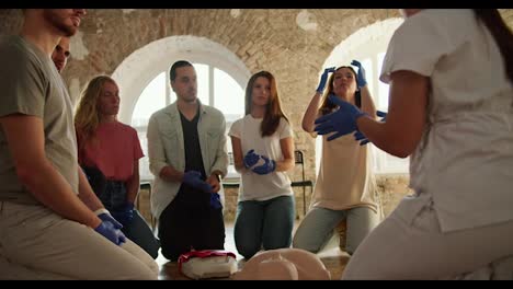 Close-up-shot:-a-group-of-people-listening-to-a-professional-nurse-at-a-first-aid-course-in-front-of-white-brick-walls-and-large-windows