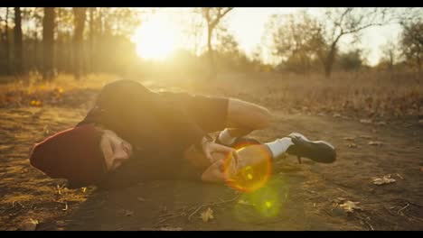 Sad-tired-guy-athletes-in-a-red-cap-in-a-black-sports-uniform-falls-to-the-ground-while-hurting-his-leg-holds-on-to-it-and-screams-while-jogging-in-the-autumn-forest-in-the-morning