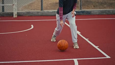 Close-up-a-blonde-girl-with-a-bob-hairstyle-in-a-blue-hat-in-a-sports-uniform-hits-an-orange-basketball-ball-from-the-red-floor-on-a-street-court-during-her-workout-during-the-day