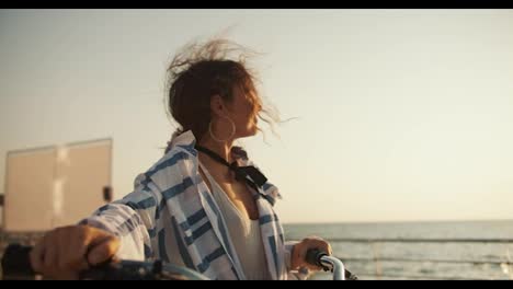 A-happy-brown-haired-girl-walks-along-the-beach-along-the-sea-and-carries-her-bicycle-next-to-her.-Girl-on-a-bike-ride-near-the-sea