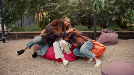 A-brunette-girl-sits-on-a-bean-bag-chair.-Three-friends-run-up-to-the-girl-and-hug-her.-Rest-in-the-country-house