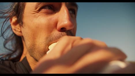 Close-up-shot-of-the-face-of-a-happy-brunette-guy-with-stubble-who-eats-a-hot-dog.-A-cheerful-guy-eats-a-hot-dog-and-smiles-during-his-day-off