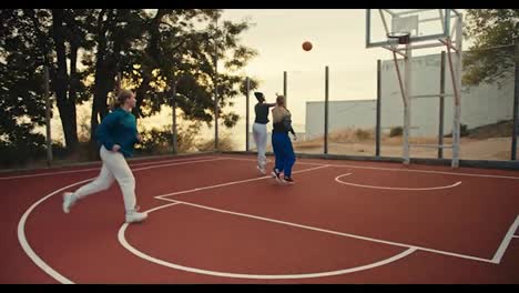 Drei-Blonde-Mädchen-Laufen-Auf-Einem-Roten-Basketballplatz-Und-Spielen-Basketball-Mit-Einem-Orangefarbenen-Basketballball-Während-Ihres-Basketballtrainings-Am-Morgen-Im-Sommer