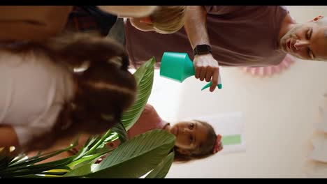 Vertical-video-of-a-man-with-gray-hair-in-a-purple-T-shirt-explaining-to-children-how-to-properly-use-a-spray-bottle-for-watering-plants-and-spraying-flowers-with-water