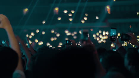 Music-fans-in-concert-hall-waving-lights-and-shooting-with-cellphones