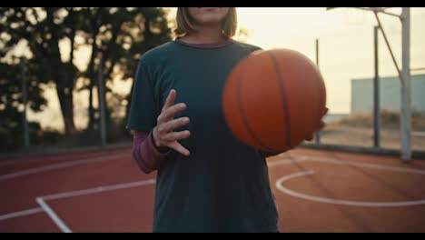 Nahaufnahme-Eines-Blonden-Mädchens-Mit-Bob-Frisur-In-Einer-Sportuniform,-Das-Beim-Morgendlichen-Basketballtraining-Auf-Einem-Straßenplatz-Einen-Orangefarbenen-Basketball-Von-Hand-Zu-Hand-Wirft