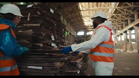 A-man-with-black-skin-and-a-beard-in-a-white-uniform-and-an-orange-vest-together-with-his-employees-sorts-waste-paper-at-a-waste-and-garbage-processing-plant