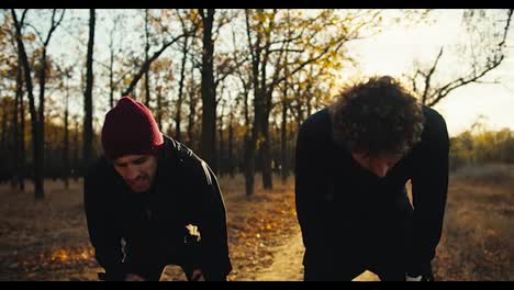 A-guy-in-a-red-cap-a-brunette-with-a-beard-in-a-black-sports-uniform-together-with-his-friend-a-man-with-curly-hair-are-running-to-their-destination-after-their-jogging-in-the-autumn-park-at-Sunrise-in-the-fall